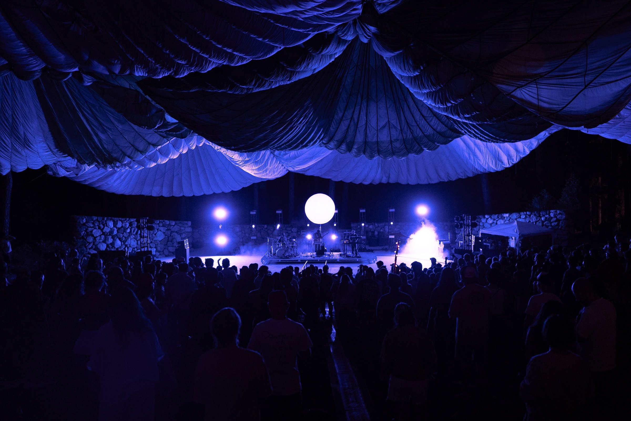 The draped tent roof lit deep blue over the crowd, the sphere small and white at the far end