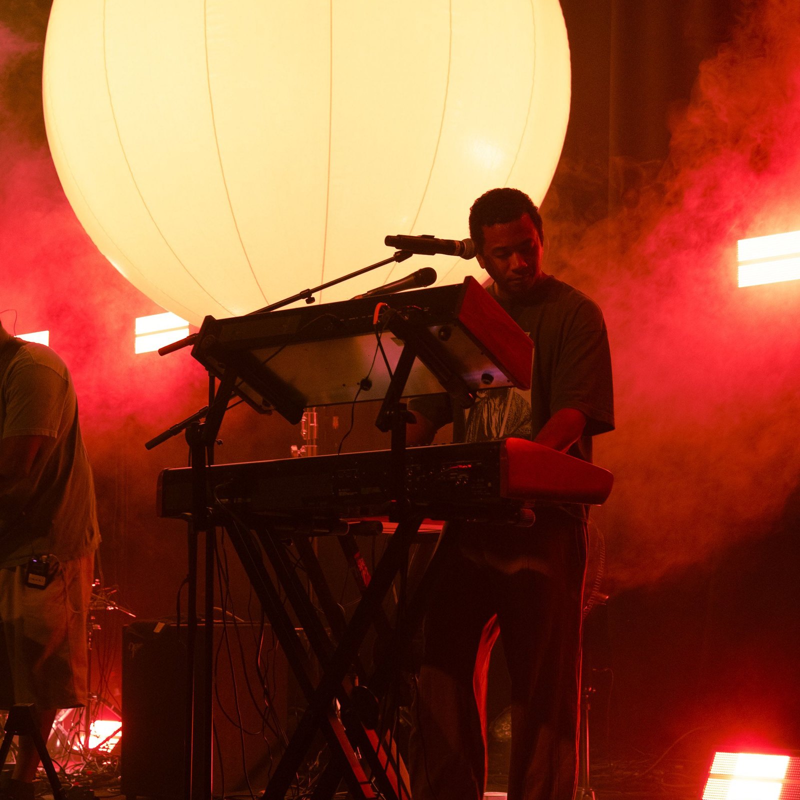 Ball on Toro y Moi's 2026 tour — Chaz Bear at the keys with the six-foot LED sphere glowing behind him through red haze