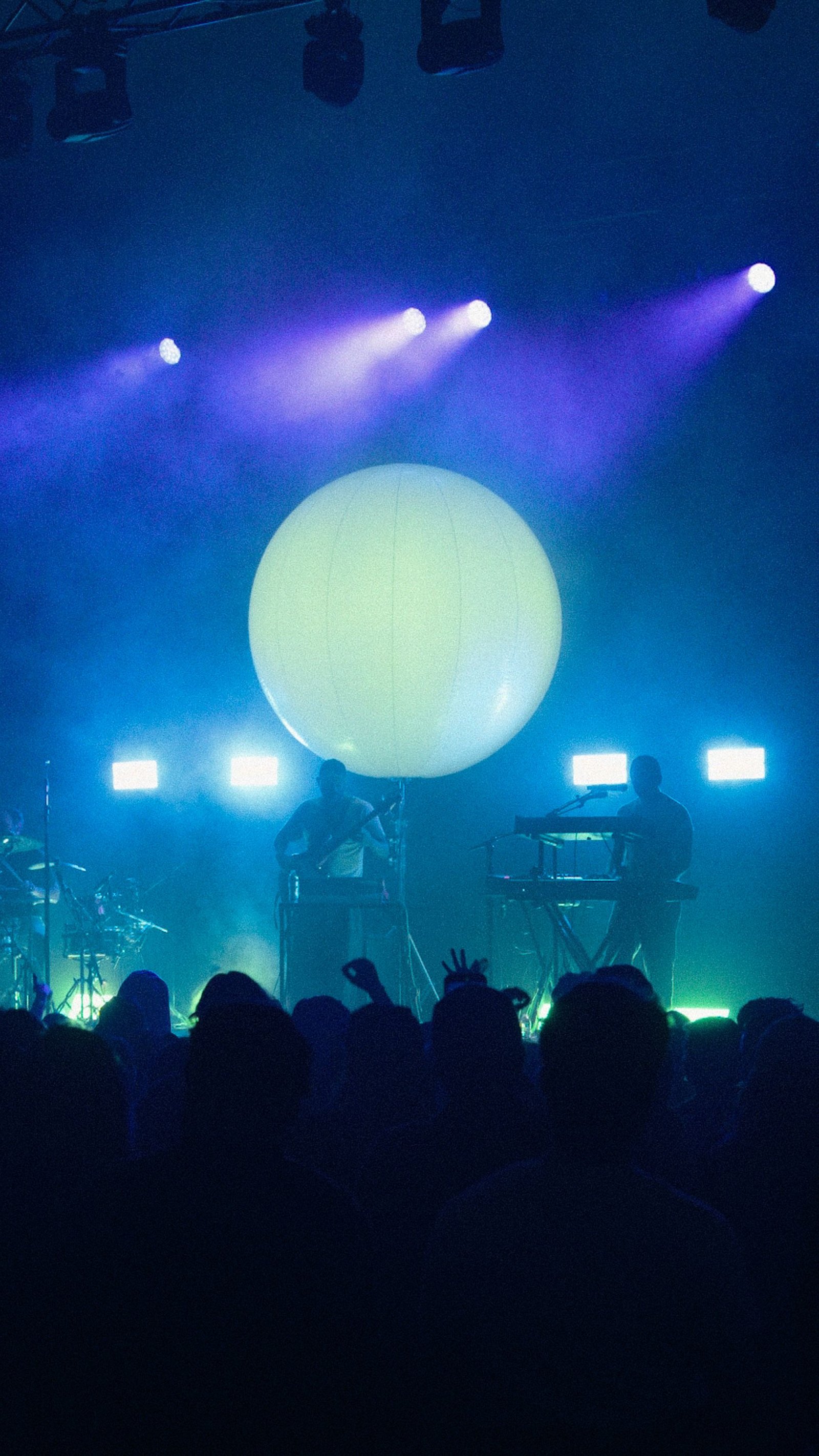 The sphere lit white above the band with the crowd silhouetted in blue and purple haze