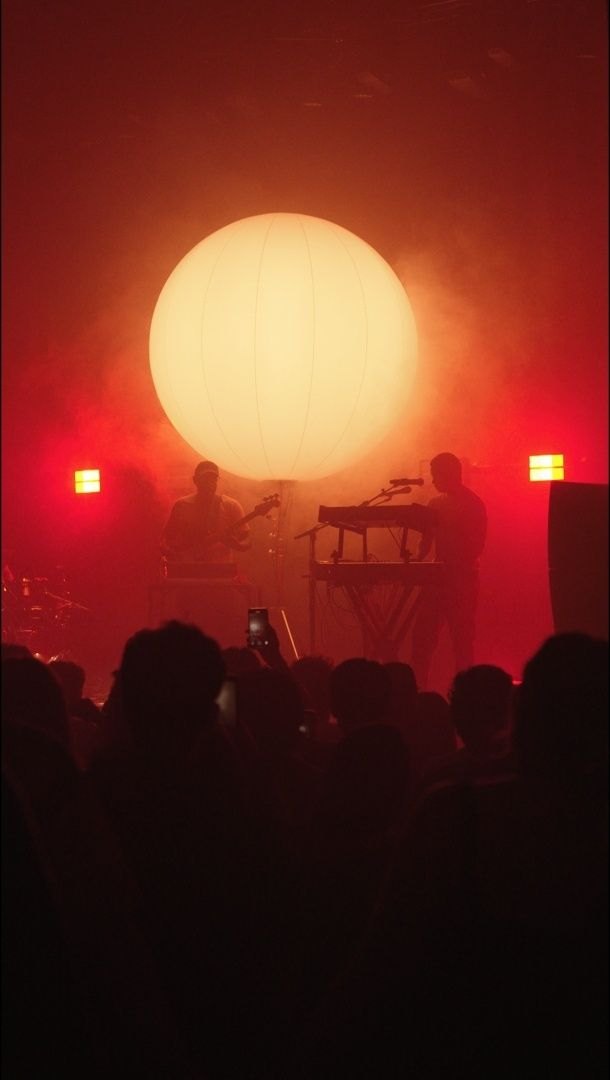 The sphere burning orange above the band, phones raised in the crowd below