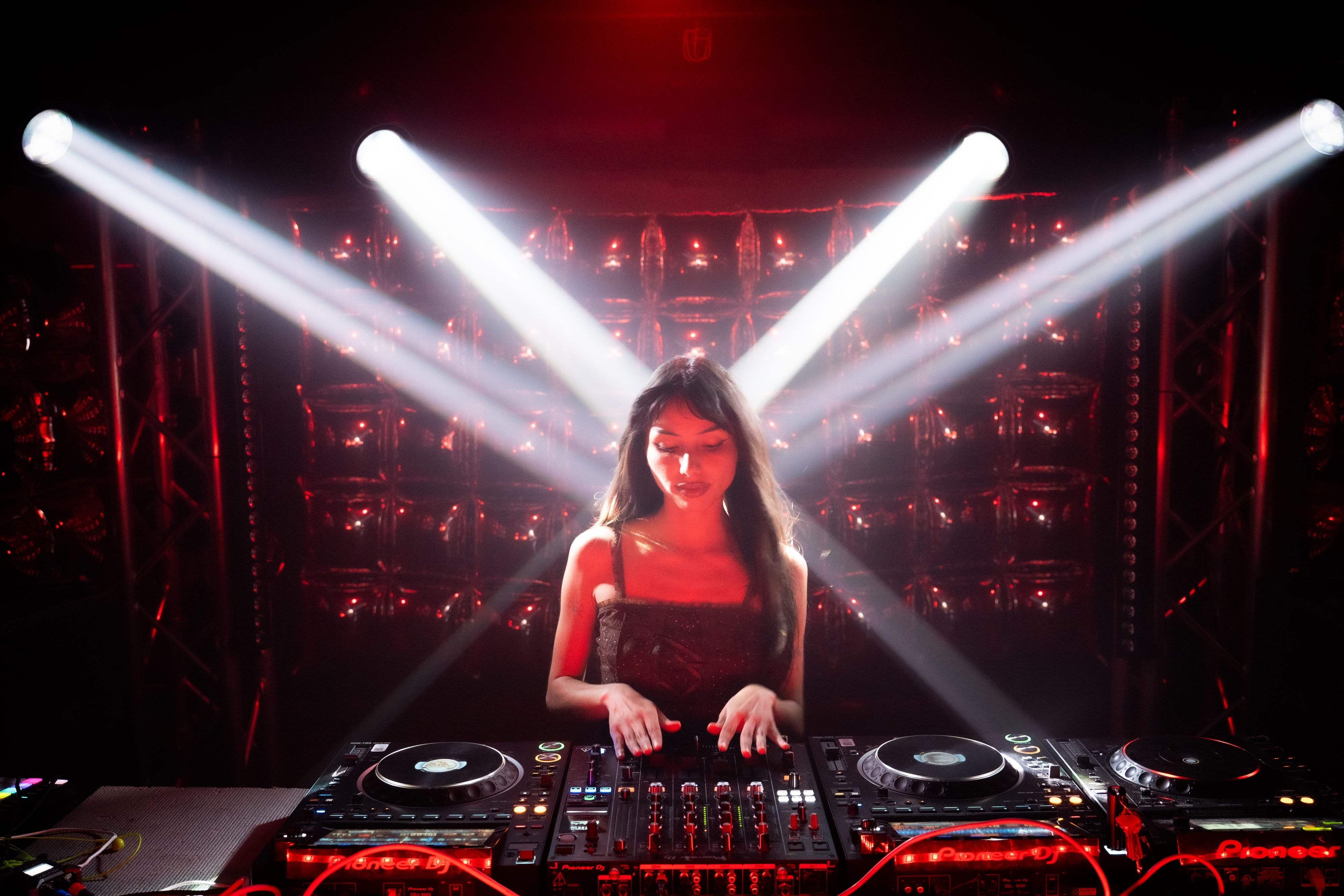 BalloonBooth at Club Six — Erika at the decks with four white moving-head beams crossing above her, the mylar balloon wall lit red behind