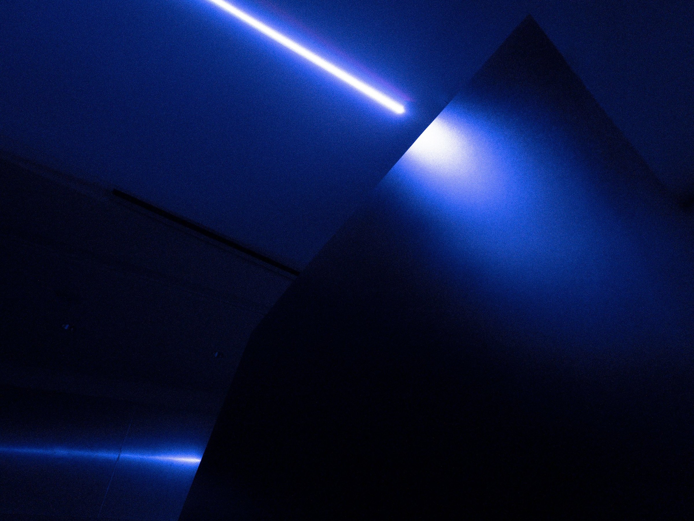 Close-up of the black acrylic column’s corner in blue light, a single laser line crossing the ceiling above it