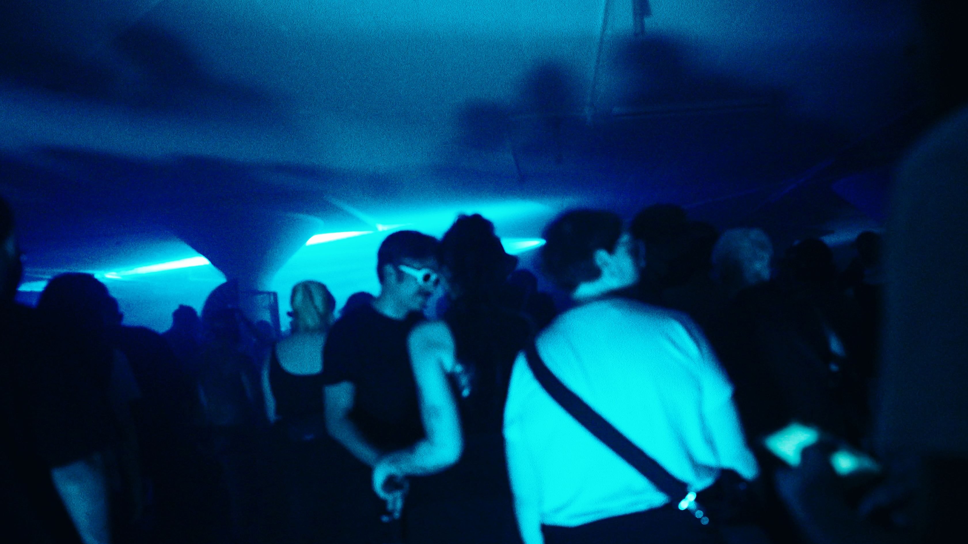 The crowd under a cyan beam running the length of the low garage ceiling