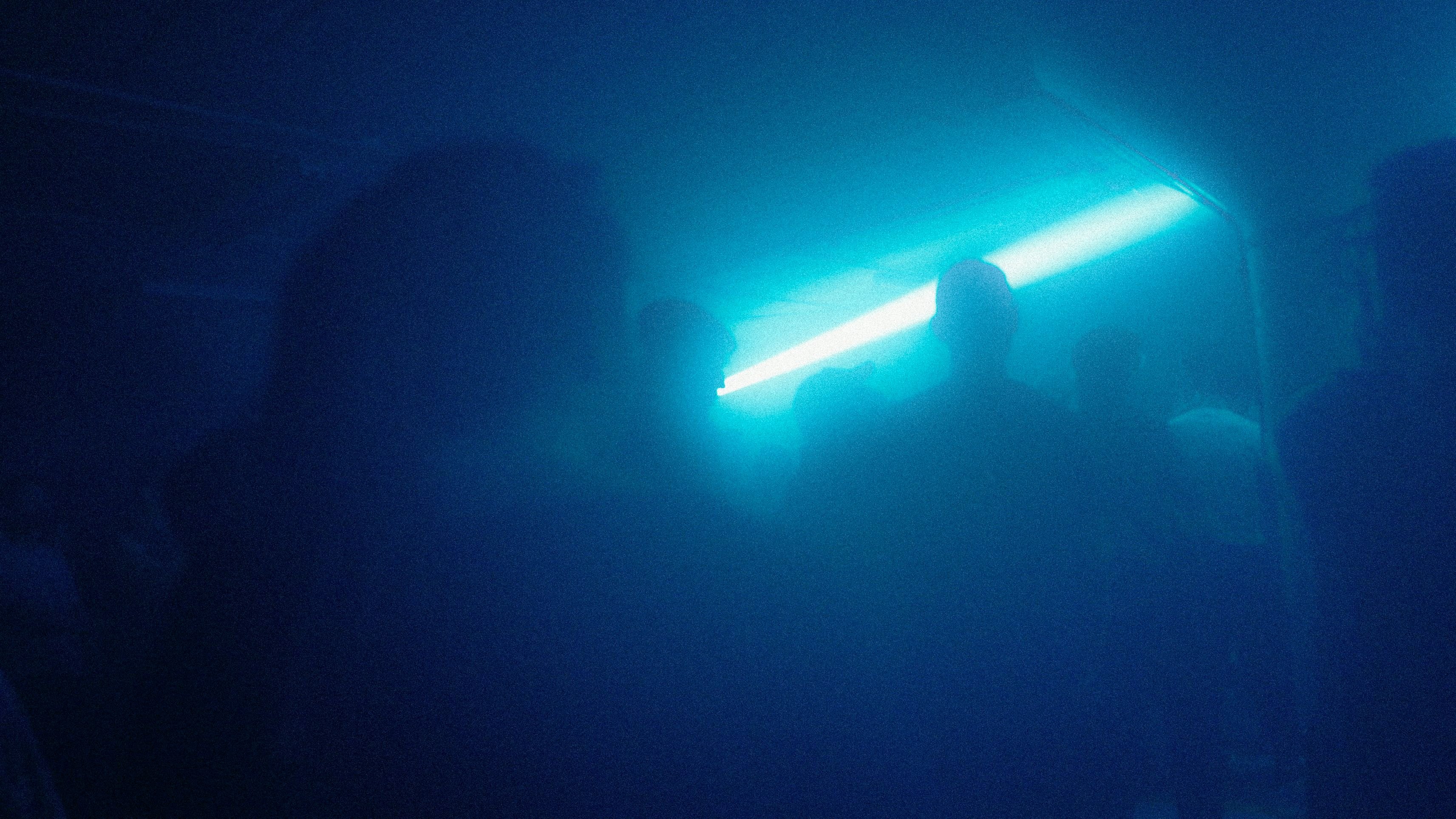A single cyan beam cutting horizontally through the fog above the heads of the crowd