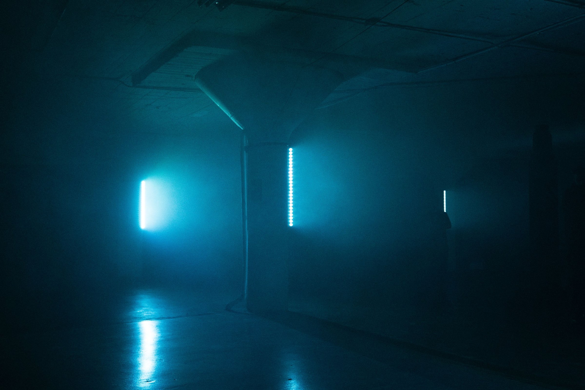 The empty garage in teal, battery strips reflecting off the concrete columns and the polished floor