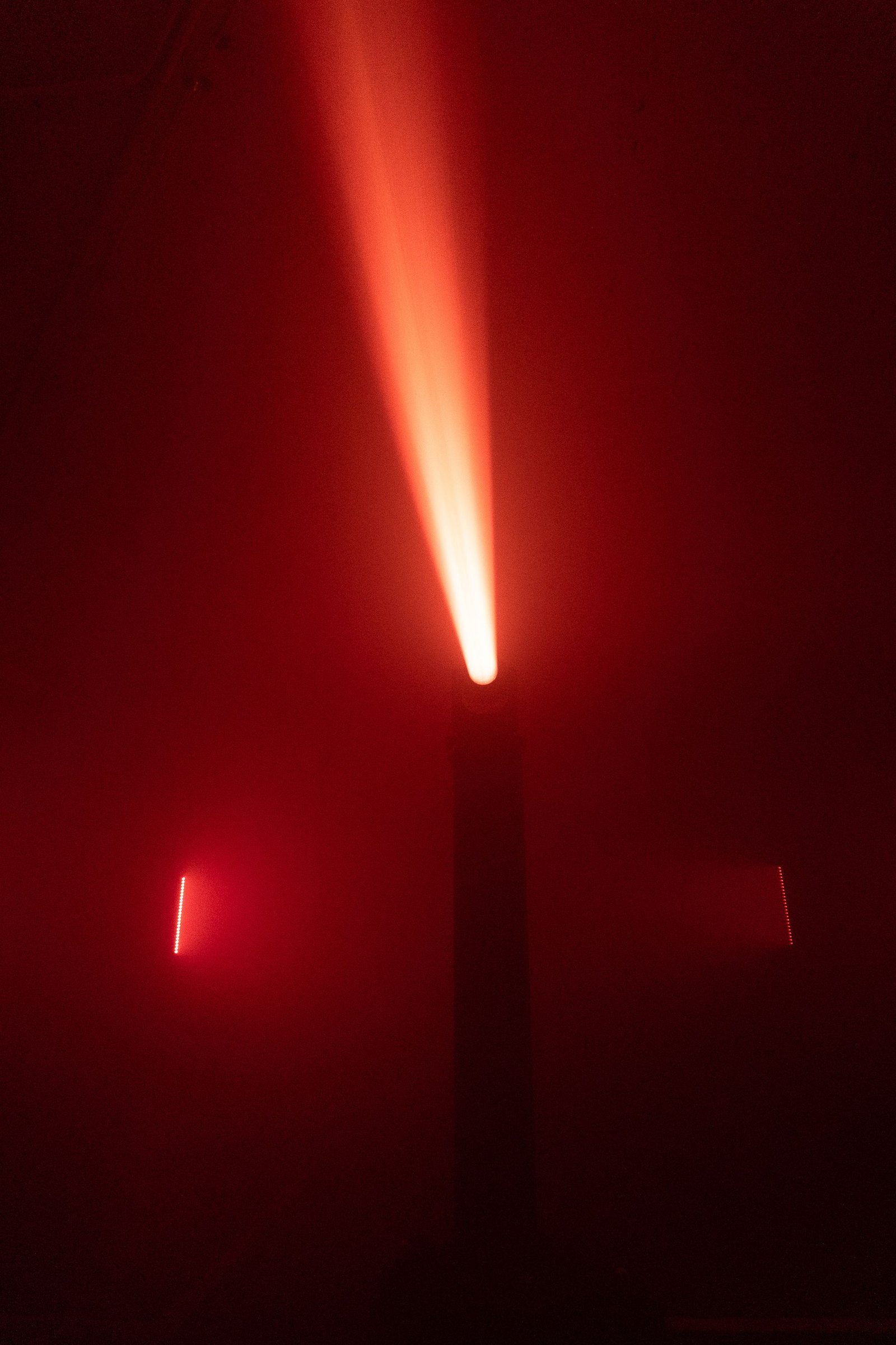 The Claypaky Sharpy throwing a single red beam upward from its truss, battery strips glowing on either side in the fog