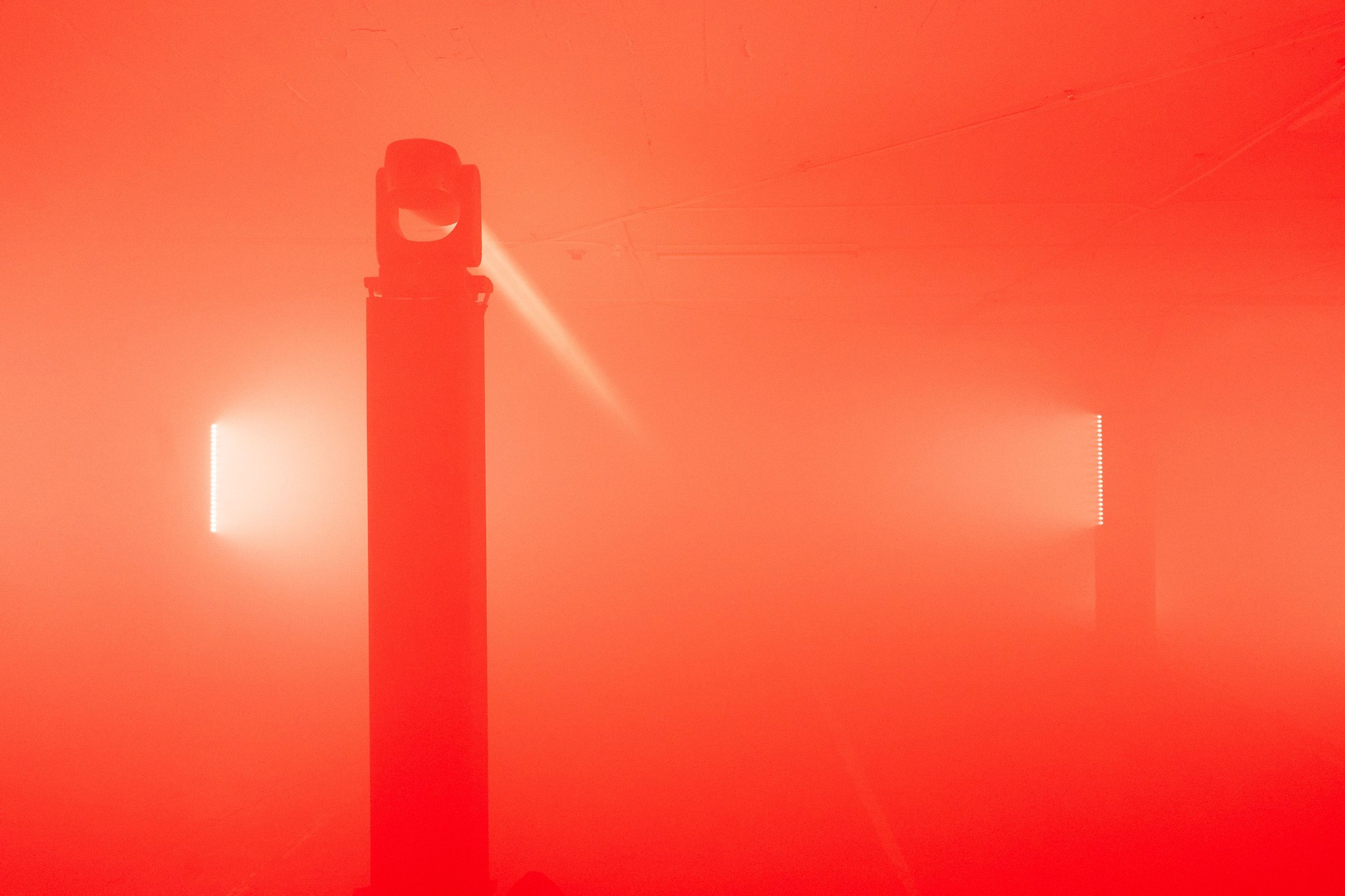 FieldWash at SVN West — the central truss and moving head in silhouette against two glowing wall panels in dense red fog
