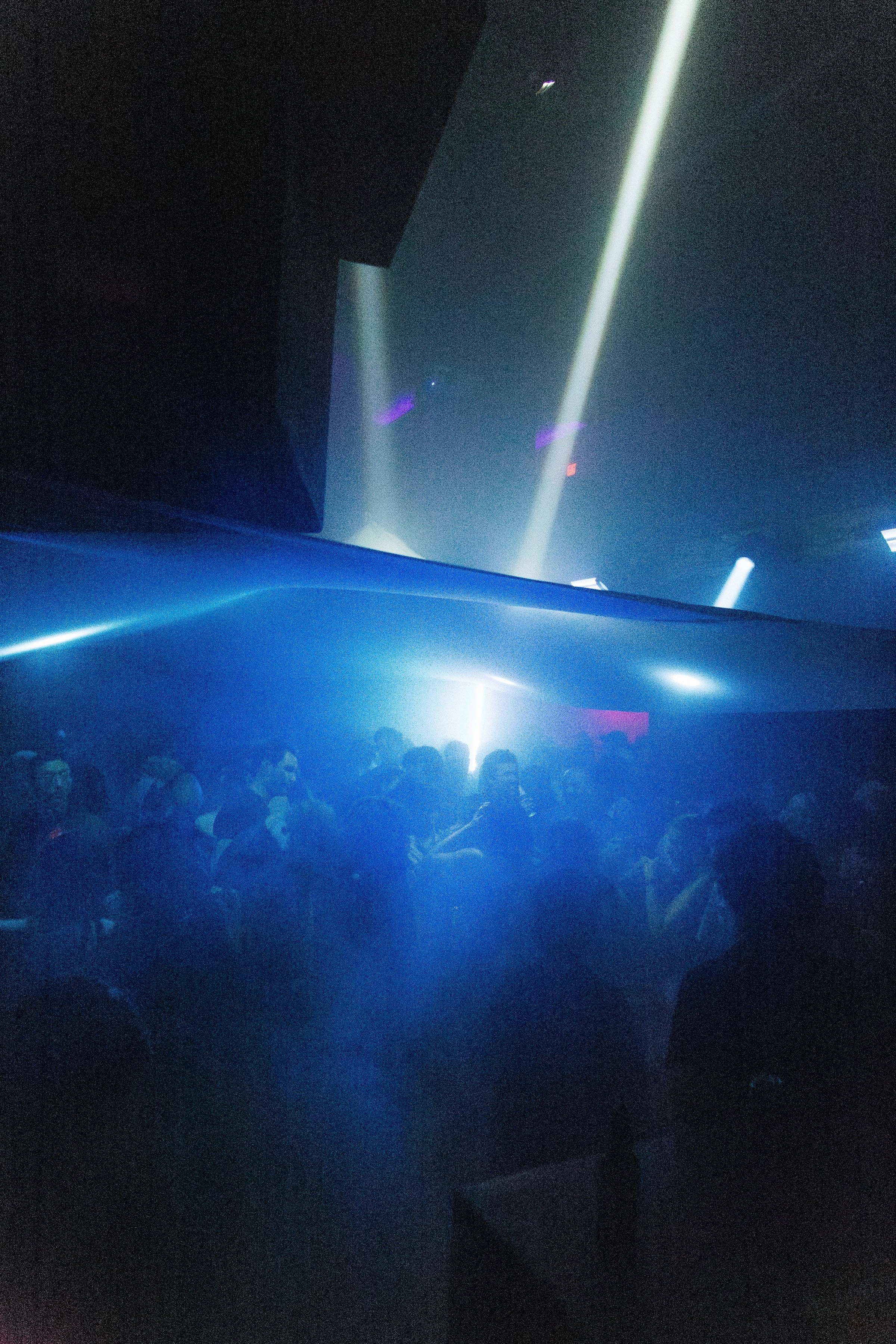 The crowd under the canopy in blue, white beams cutting down past the fabric's edge