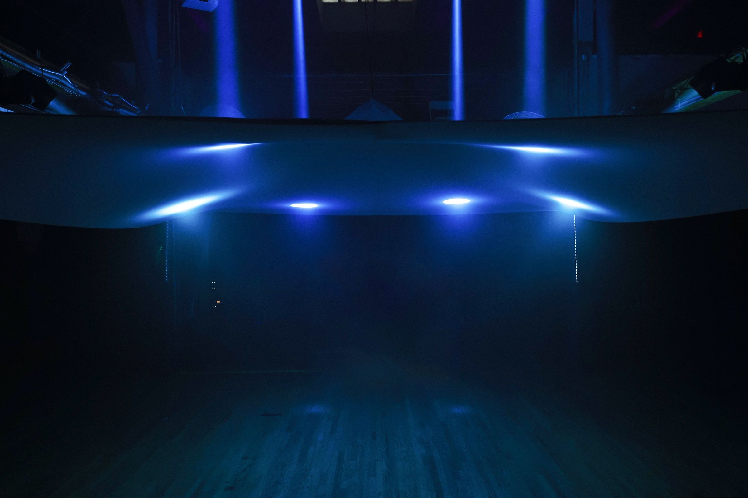 The empty dance floor under the canopy, ice blue beams landing along the fabric's catenary curve