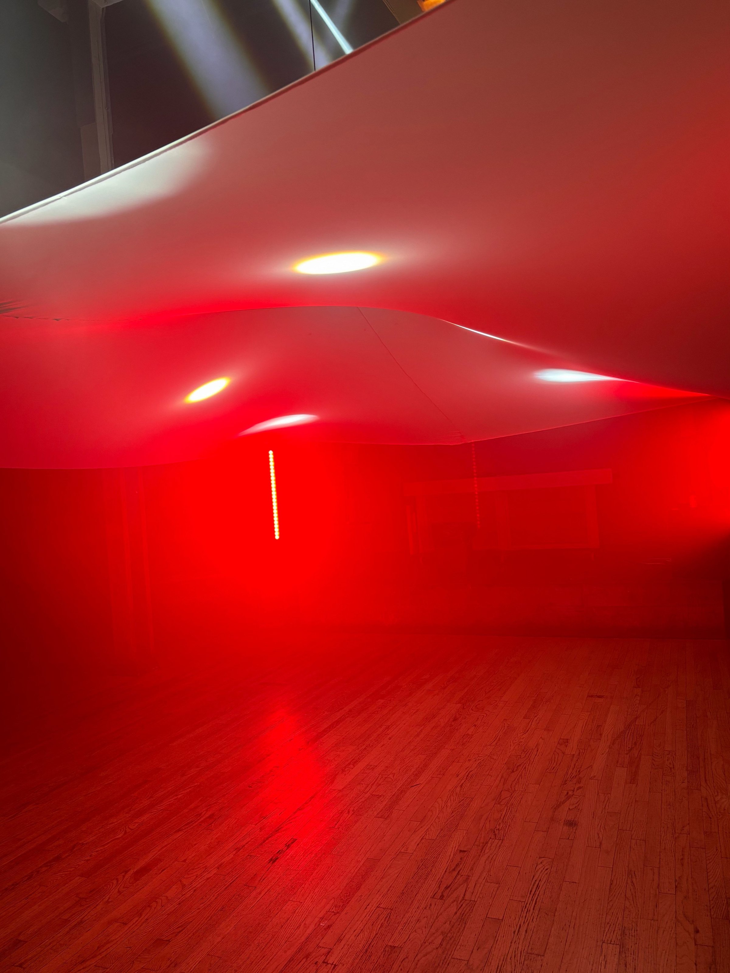 The canopy stretched low over the empty dance floor, lit deep red, its catenary curve catching four spots of light with the wood floor below