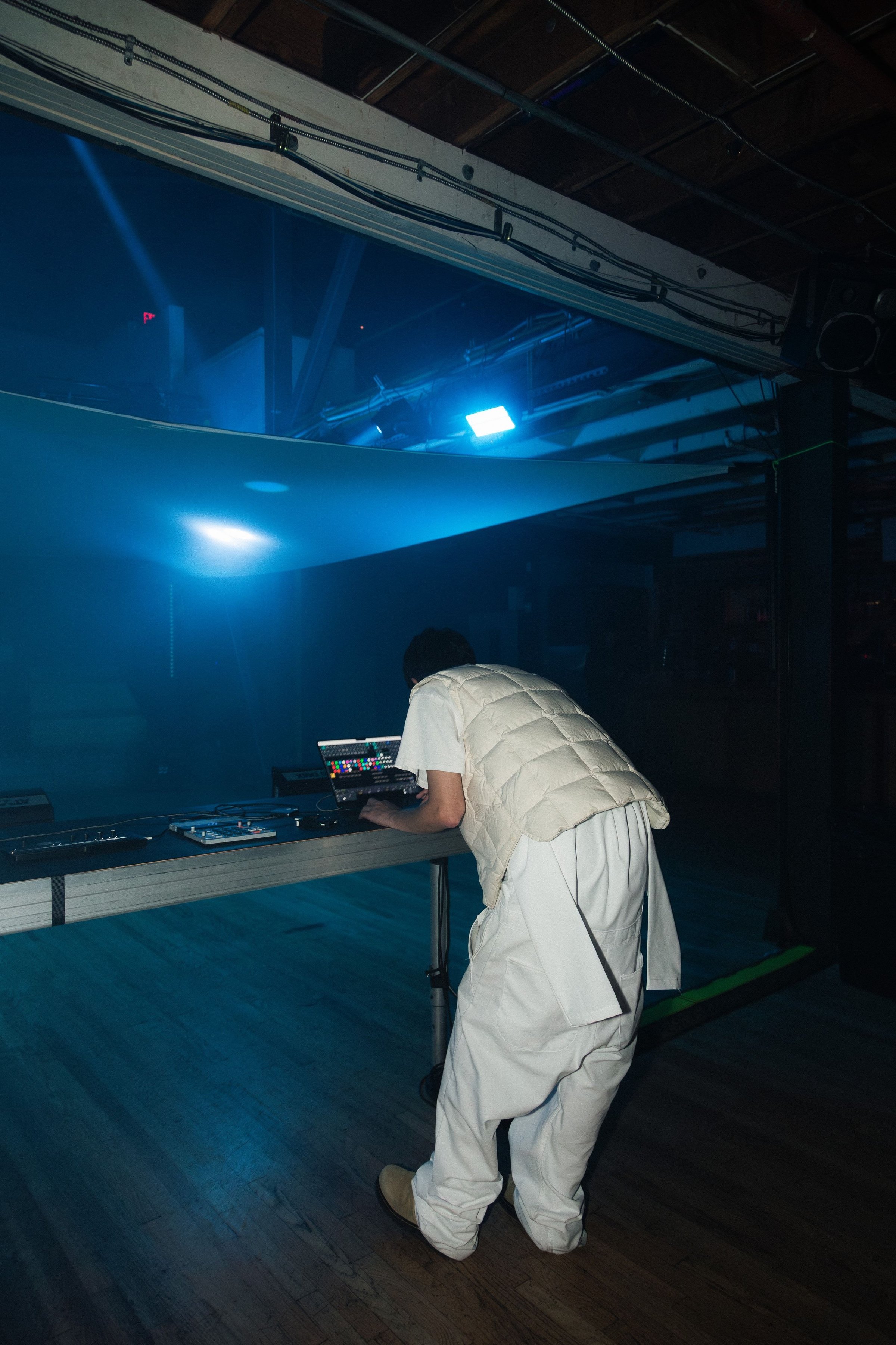 An operator in a white puffer leaning over the Teenage Engineering gear, the room lit blue behind