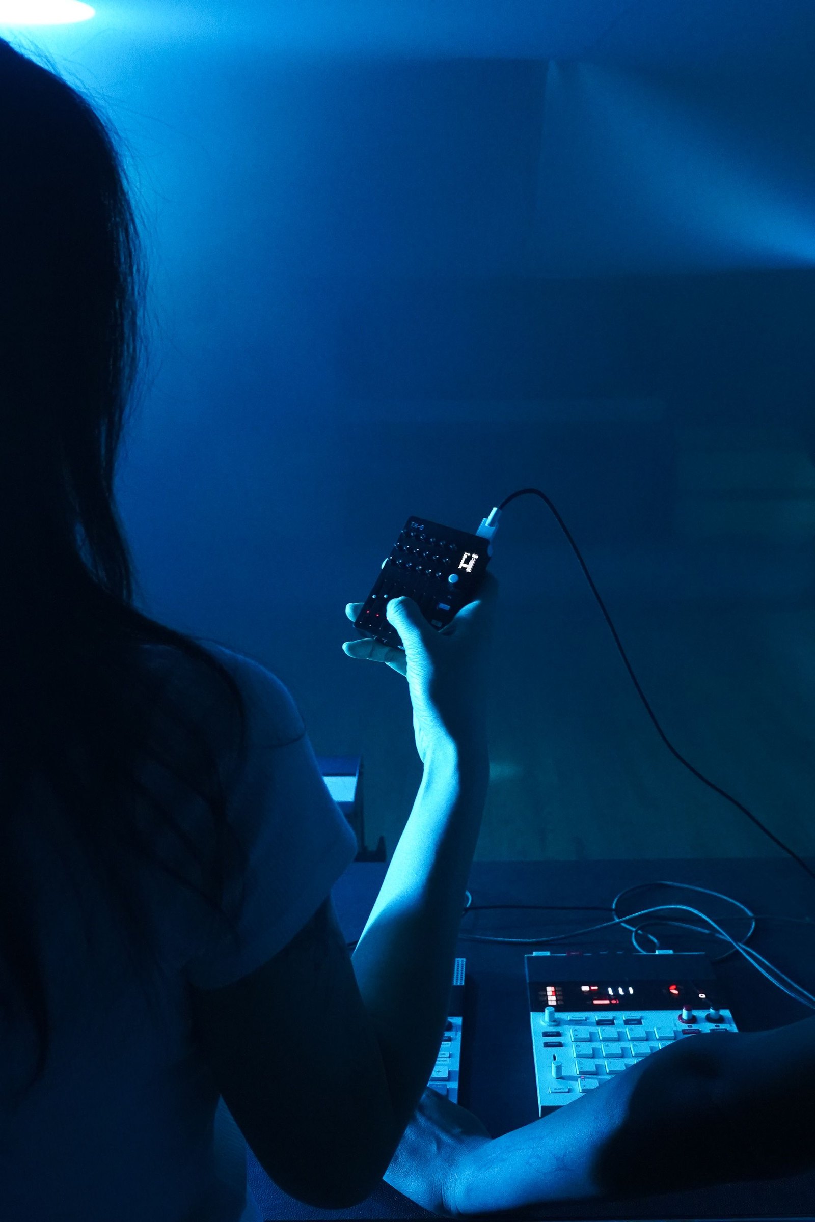 A hand holding a Teenage Engineering TX-6 above the lighting table in blue light