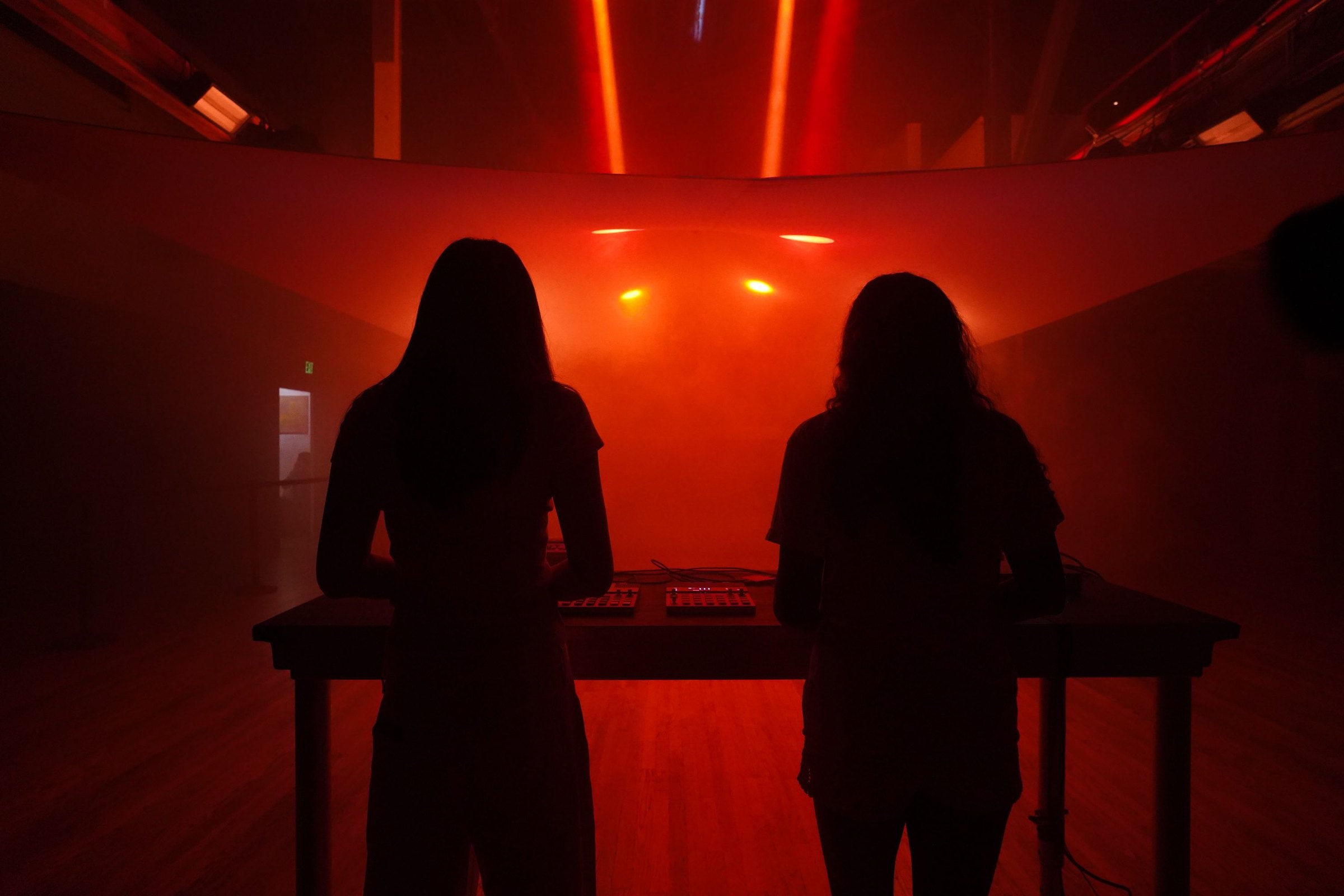 Two operators silhouetted at the lighting table under a red wash, the empty room behind them