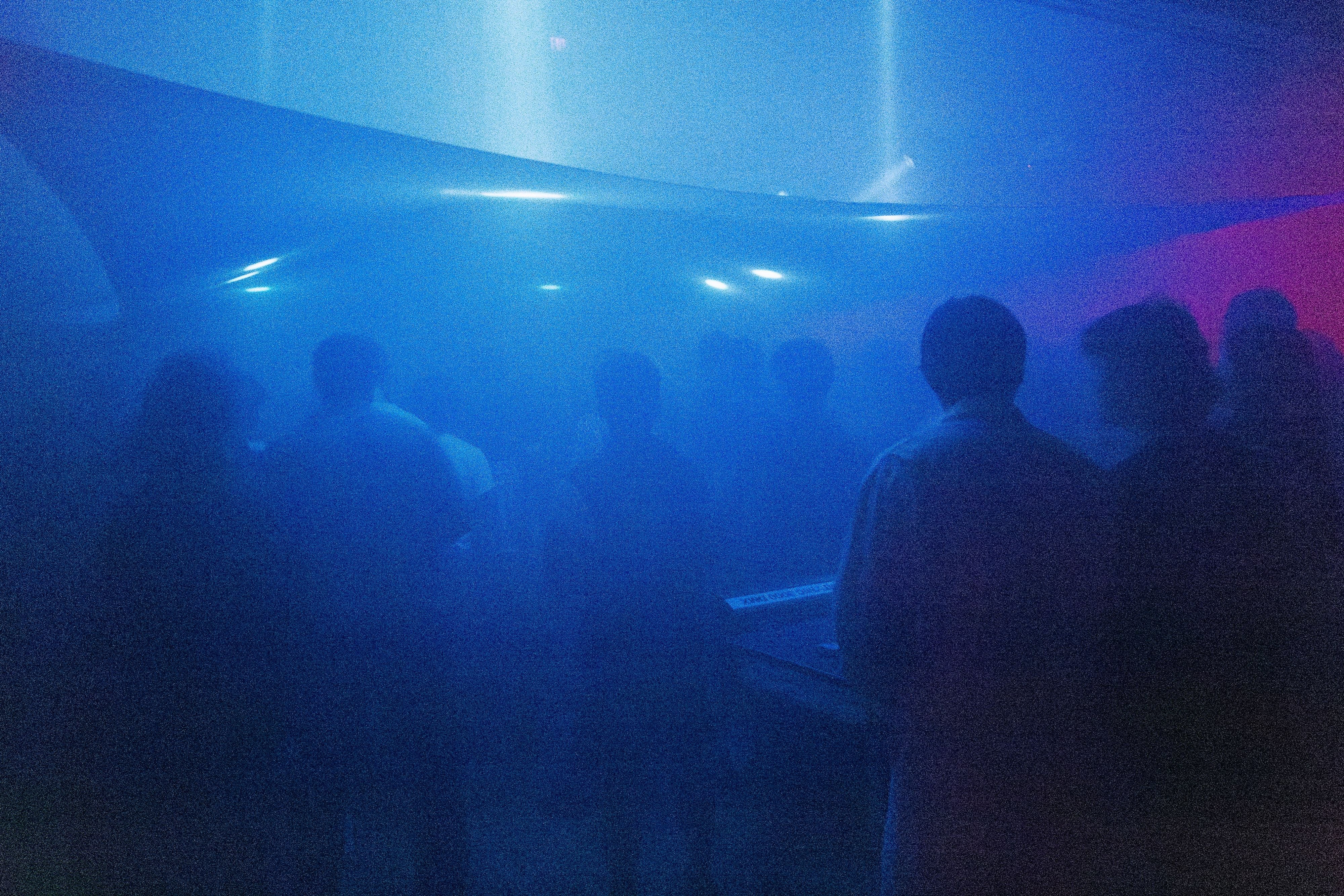 The lighting team at their table with their backs to the camera, the blue-lit crowd in front of them