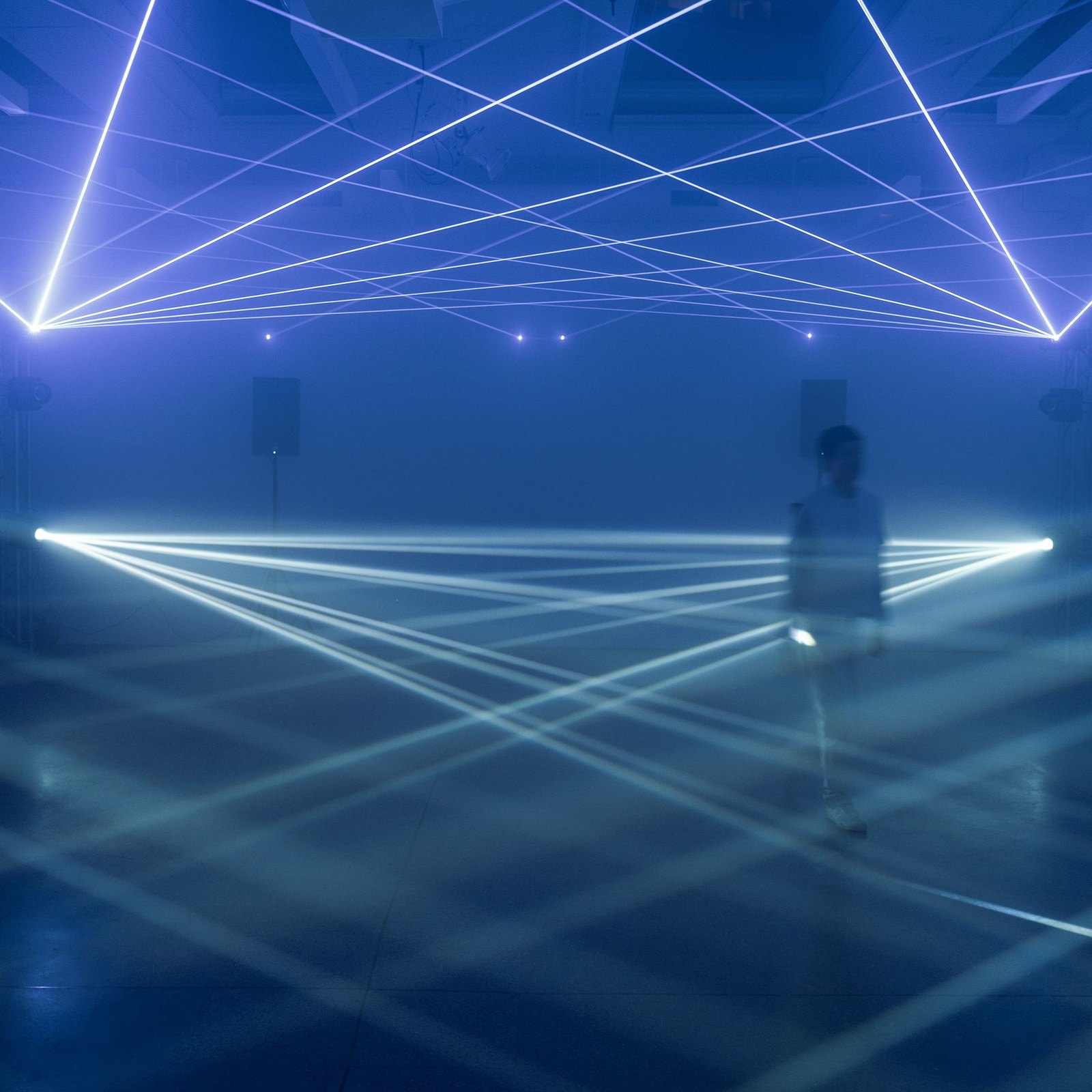 Lattice at Four One Nine — a lone figure in the fog beneath a grid of laser lines crossing overhead and fanning low across the floor