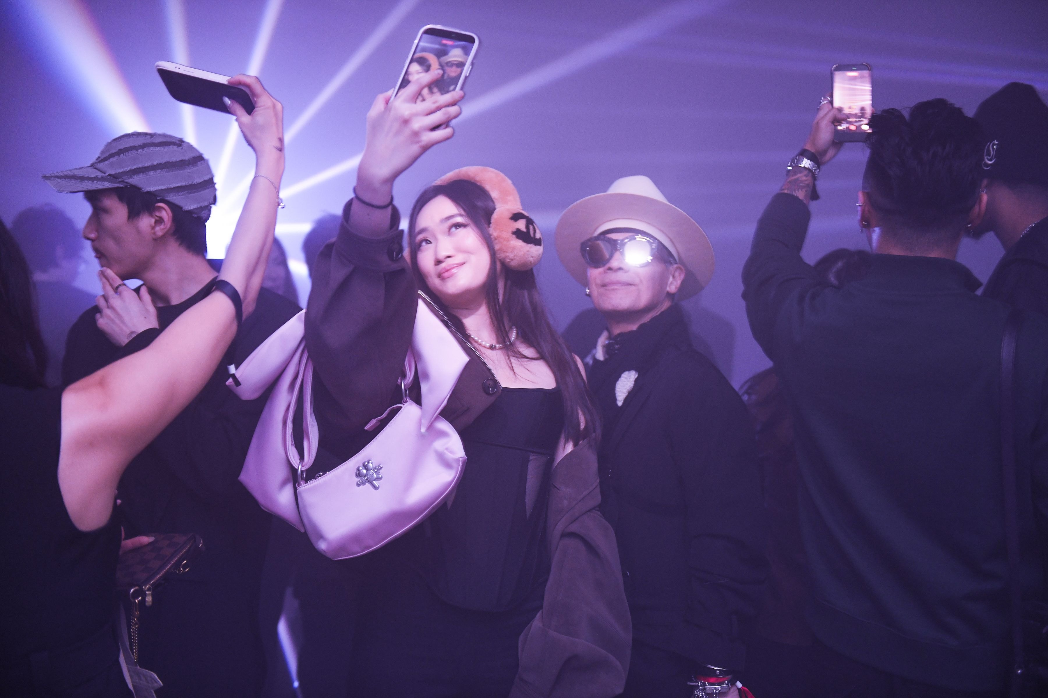Attendees holding phones up to photograph each other under the lasers, one in a white hat and sunglasses