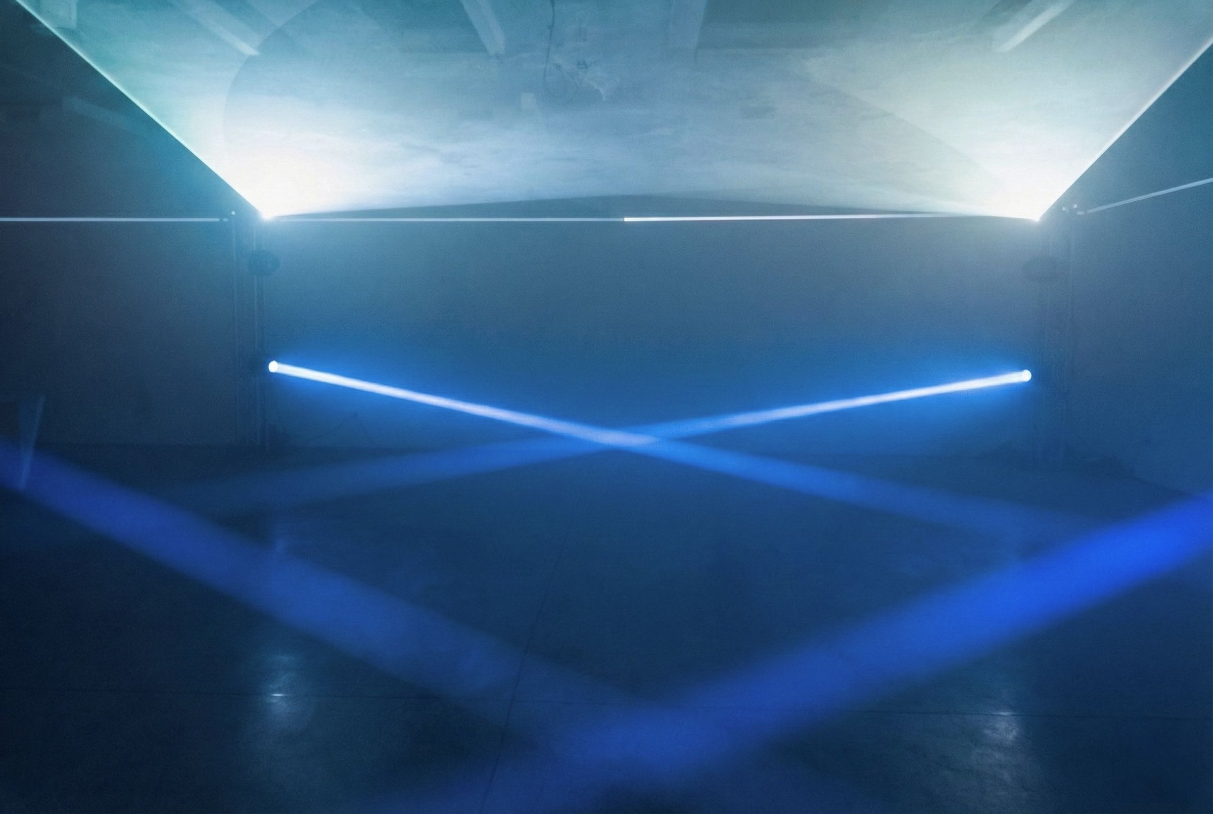 The empty room before the party, two blue laser lines crossing in an X above the floor and beams grazing the side walls