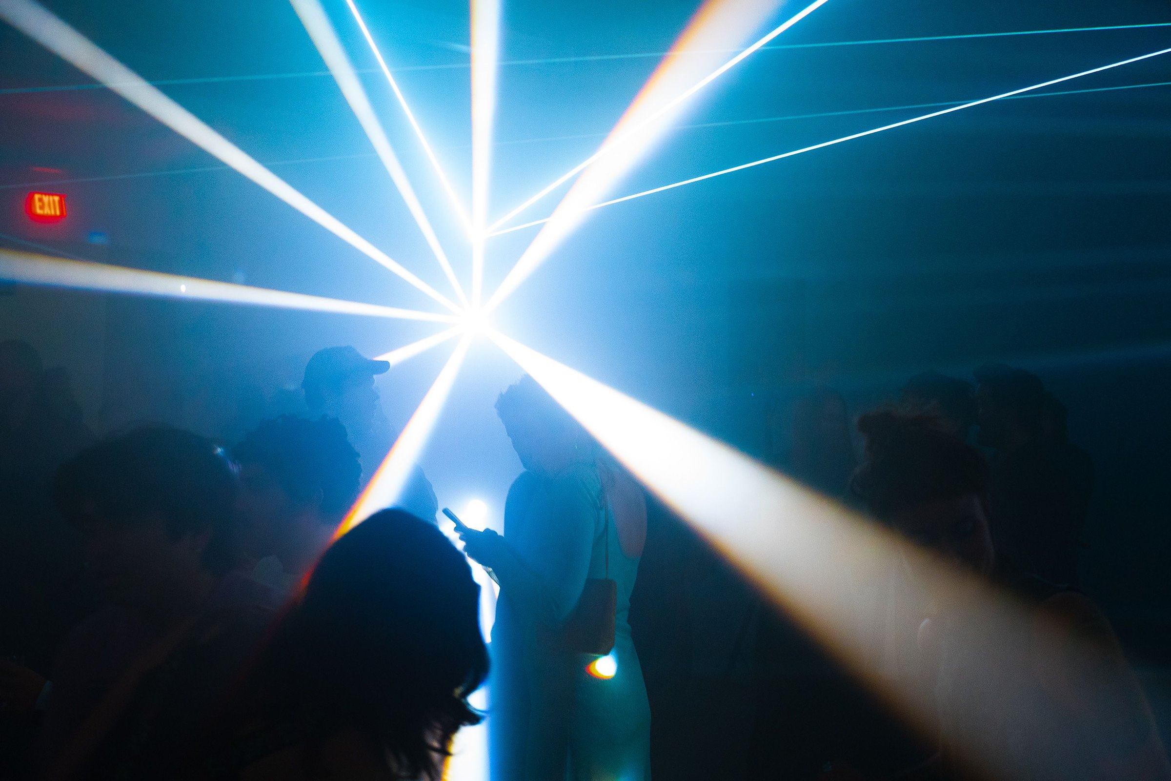 A radial starburst of white laser beams bursting from a single point above the heads of the crowd